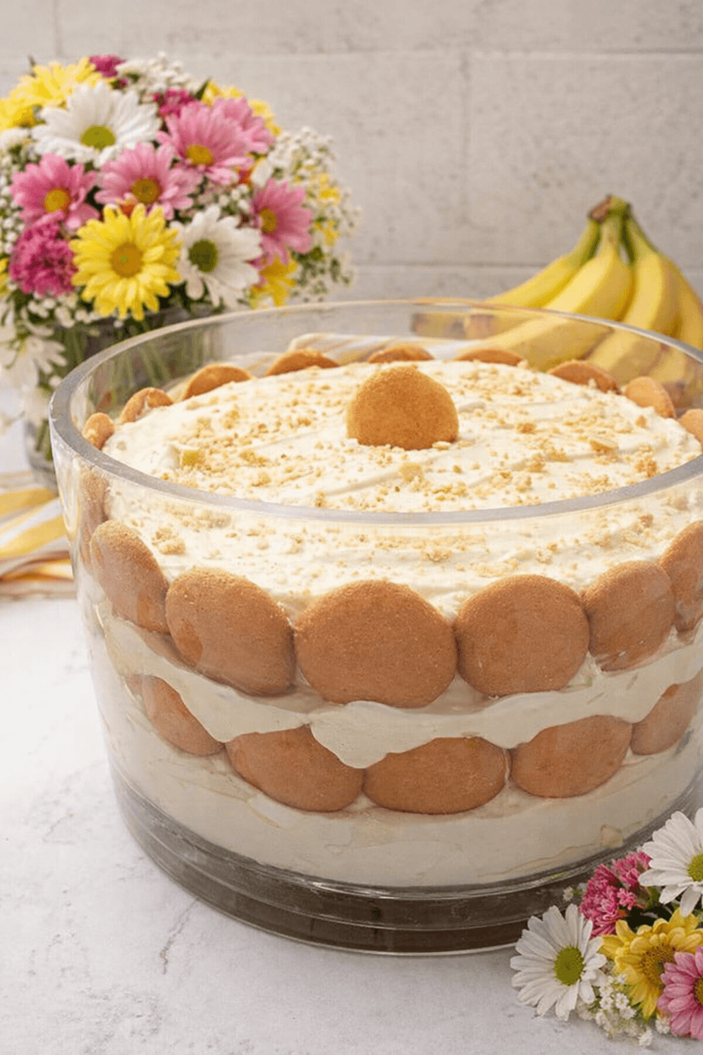 Layered banana pudding trifle in a glass bowl with vanilla wafers and colorful spring flowers.