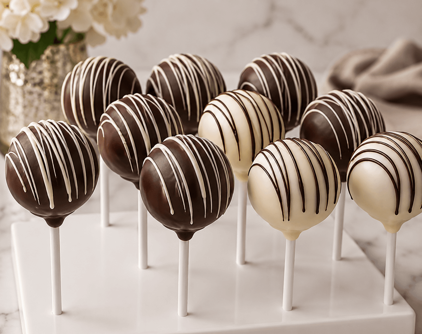 Dark and white chocolate cake pops with decorative drizzles arranged on a white stand.