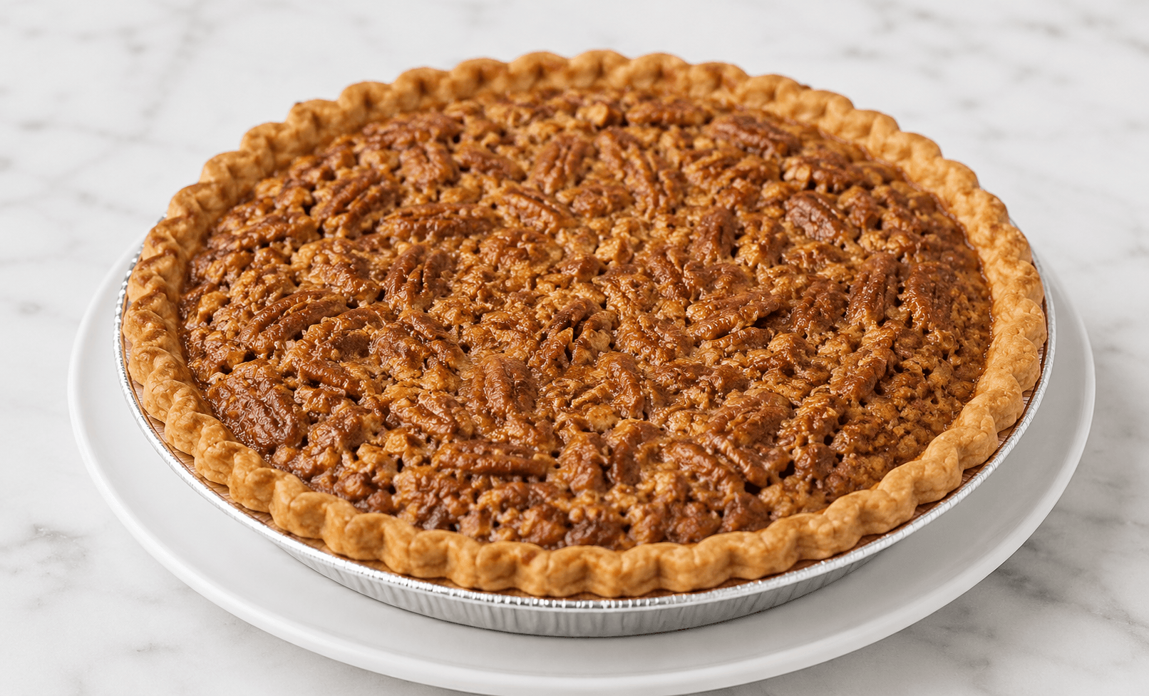Whole pecan pie with a fluted crust on a white plate and marble surface.