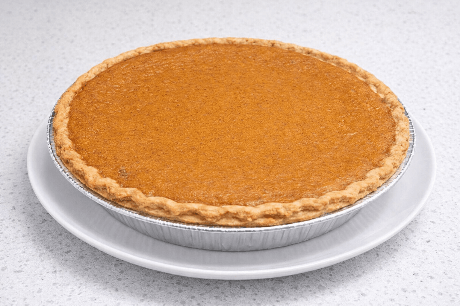Whole pumpkin pie with a fluted crust in a foil tin on a white plate.